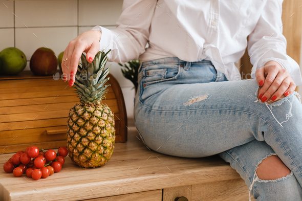 a close-up of a housewife in a white shirt and jeans is sitting on a table and fruits - Stock Photo - Images