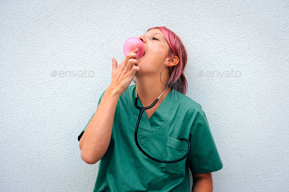 female doctor with pink hair plays with bubble gum. Funny moment at work.