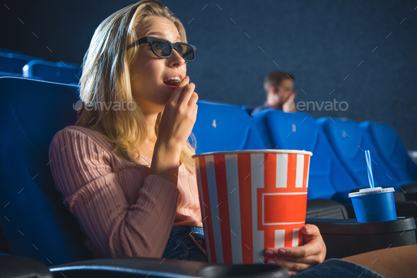 side view of young woman in 3d glasses with popcorn watching film alone in cinema