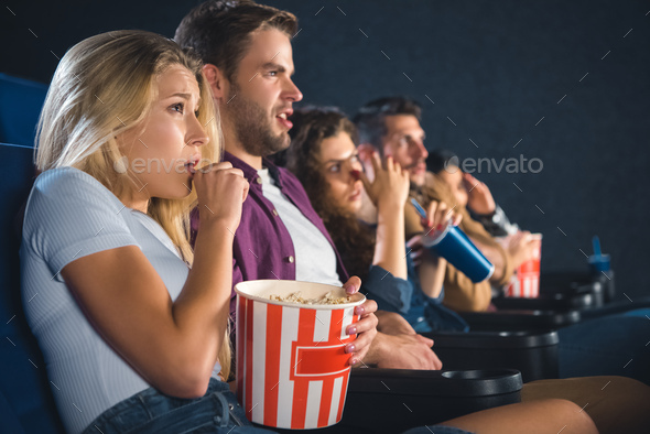 scared multiethnic friends with popcorn watching film together in movie theater