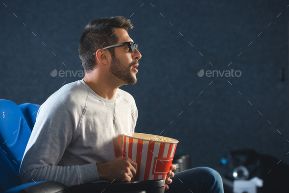 side view of emotional man in 3d glasses with popcorn watching film alone in cinema