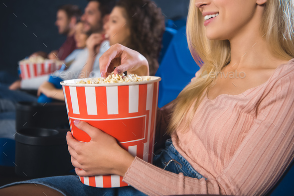 partial view of multiethnic friends with popcorn watching film together in movie theater