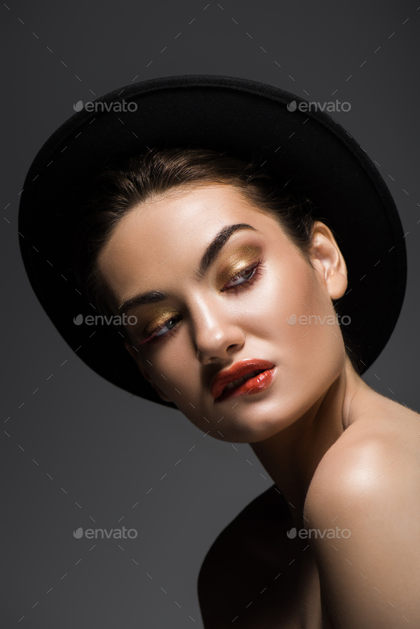 beautiful seductive girl in black felt hat biting lip, isolated on grey