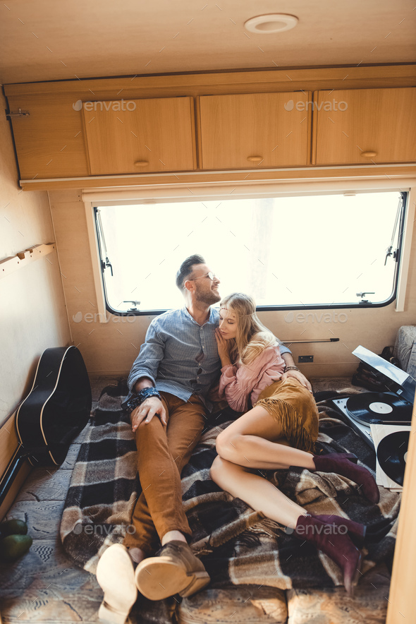 beautiful couple hugging and resting inside campervan with acoustic guitar and vinyl records