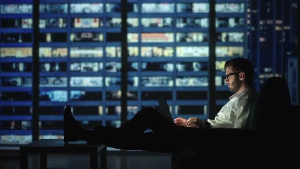 Focused Young Man Lying on the Sofa As He Works on His Laptop Late Into the Night alt