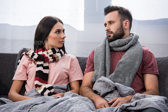 sick young couple sitting on couch and looking at each other - Stock Photo - Images