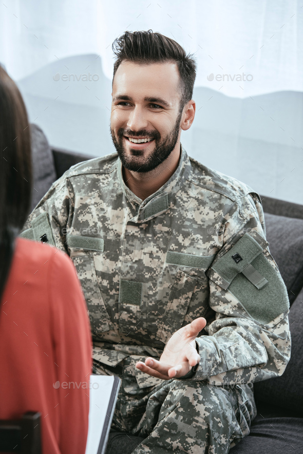 smiling soldier talking at psychiatrist and gesturing while sitting on couch during therapy session - Stock Photo - Images