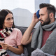 sick young couple with electric thermometer and ice pack sitting together on couch - PhotoDune Item for Sale
