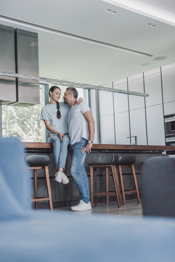 low angle view of attractive woman sitting on kitchen counter and embracing boyfriend at home - Stock Photo - Images
