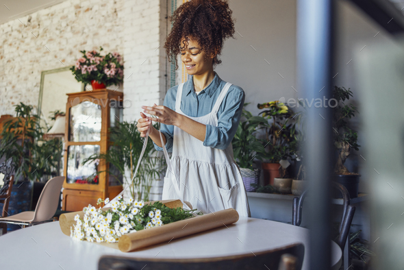 Young florist in apron creating beautiful simple daisy bouquet in craft paper - Stock Photo - Images