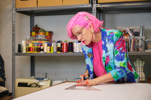 Tailor with pink hair and colorfull clothes drawing sewing patterns. - Stock Photo - Images
