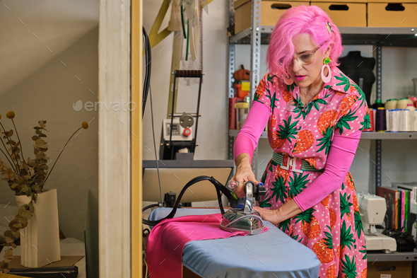 Tailor with pink hair and colorfull clothes ironing fabric. - Stock Photo - Images