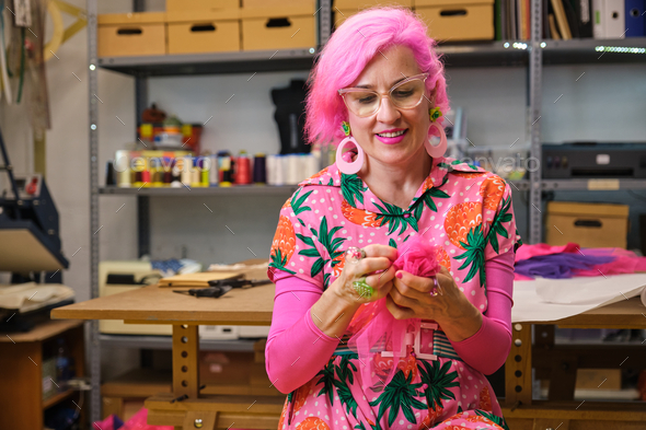 Seamstress with pink hair and colorfull clothes hand sewing a piece of fabric. - Stock Photo - Images