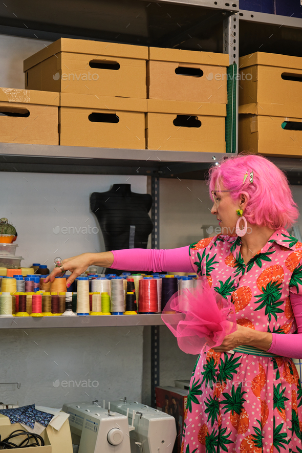 Dressmaker with pink hair and colorfull clothes choosing a thread. - Stock Photo - Images
