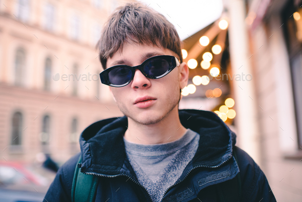 Stylish handsome teen guy wear sunglasses outdoor over city lights