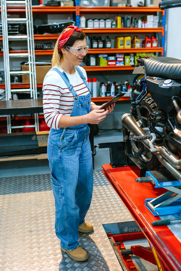 Mechanic with security glasses and digital tablet review motorcycle documentation on garage - Stock Photo - Images