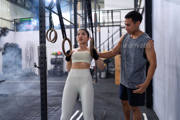 Male fitness instructor help woman doing pull-ups ring dips in a gym on gymnastic rings.