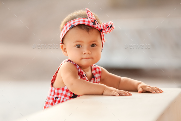Lifestyle portrait of infant baby girl standing and holding on to a bench on 4th of July day - Stock Photo - Images