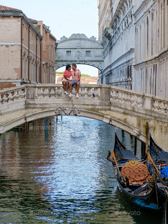 couple of men and women on a city trip in Venice Ital sitting at waterfront of the bridge of sighs - Stock Photo - Images
