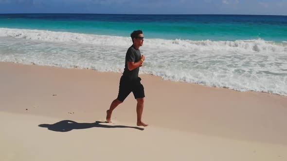 Athletic Man Run Along Ocean Surf By Sandy Beach