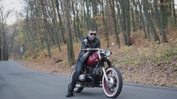 Portrait of Brutal Biker in Sunglasses and Leather on Motorcycle on Roadway alt