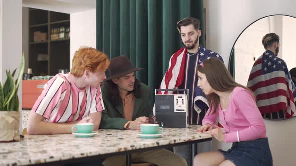 Disappointed Young Men and Women Listening to Retro Tape Recorder in Vintage Cafe Indoors alt