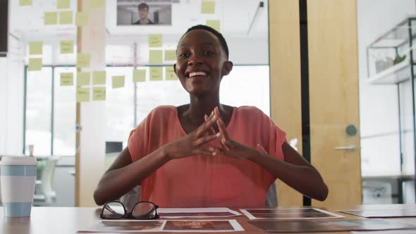 Smiling african american businesswoman at desk talking and gesturing during video call in office alt