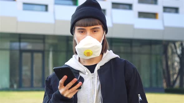 Young Female in Protection Mask Holding Smartphone and Looking To Camera alt