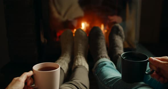 Couple Warm Up Feet in Woolen Socks By Fireplace Flame Drinking Tea in Cozy Room