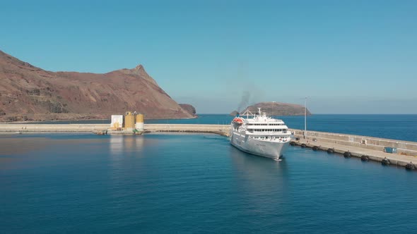 Aerial shot over Passenger boat leaving marina with island cliffs as background alt