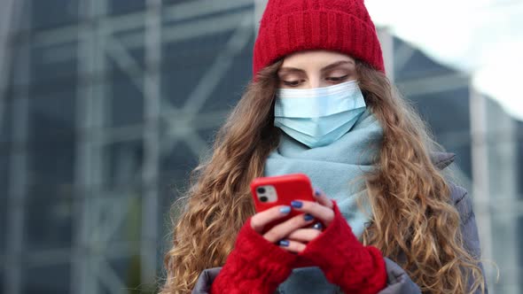Close up Portrait of Young Curly Hair Female in Medical Mask Texting on Cellphone Being Online