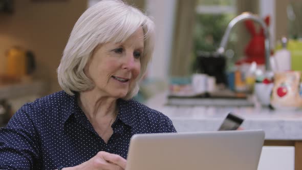 Senior woman buying online with credit card using laptop on kitchen table