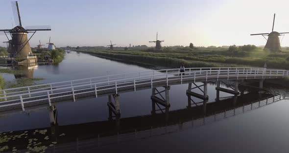 A drone shot panning left, around a girl walking and turning around on a bridge, looking at Dutch Wi alt