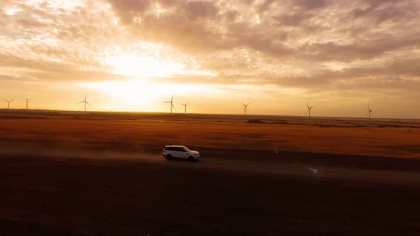 Aerial View Car Drives in Field Against Backdrop Windmill and Beautiful Sunset alt