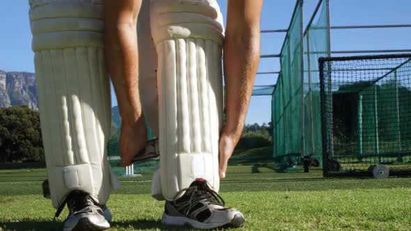Cricket player tying his batting pads during a practice session alt