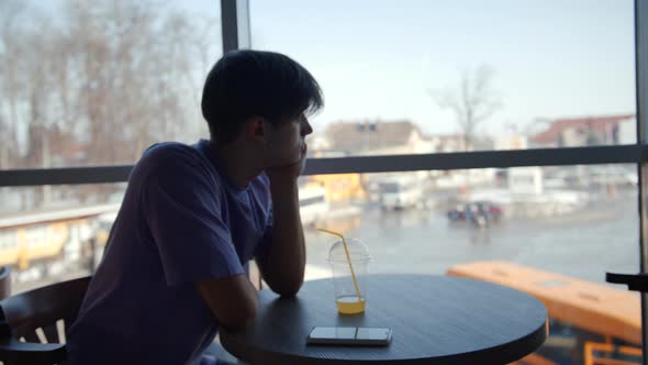 A Handsome Young Man Drinks a Healthy Orange Smoothie in a Cafe