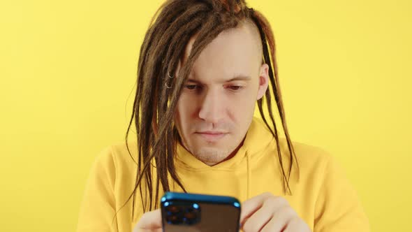 Young Serious Man Browsing Mobile Phone on Yellow Background alt