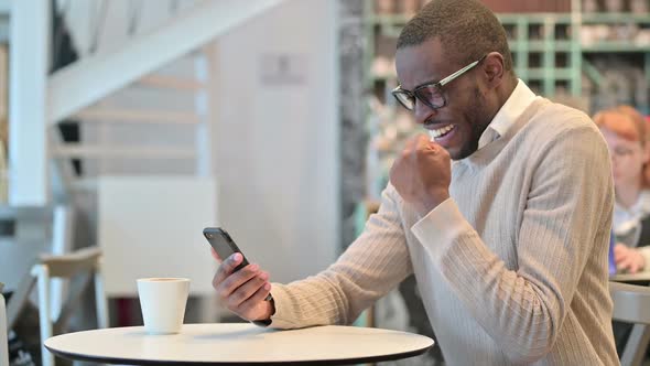 Ambitious African Man Celebrating Success on Smart Phone alt