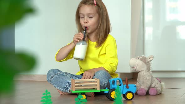 Little Happy Child Drinks Milk From Bottle with Straw Delivered By Toy Tractor in Cart