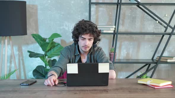 Young Curly Haired Man Using Laptop Computer with Headset to Talking Online alt