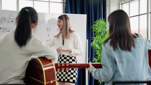 young Asian music teacher is teaching note reading and guitar chords correctly