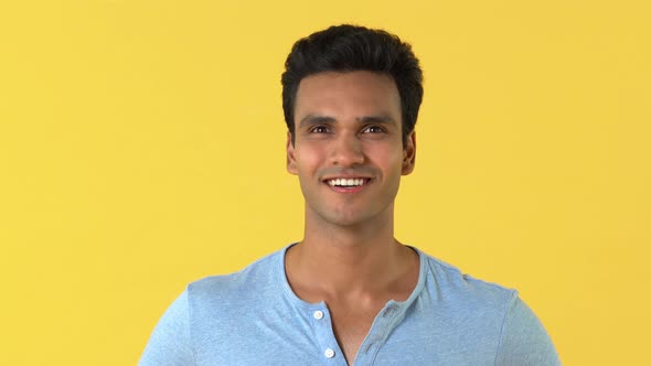 Young happy Indian man in plain gray t-shirt smiling and laughing isolated on yellow background