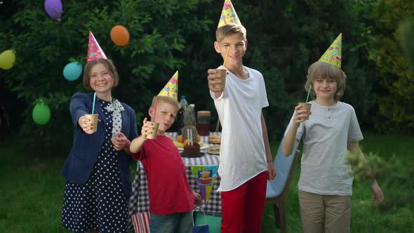 Front View Happy Children Toasting Looking at Camera Drinking Juice in Slow Motion alt