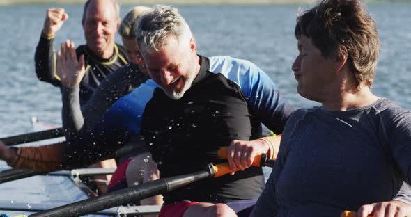 Four senior caucasian men and women in rowing boat raising hands and cheering alt