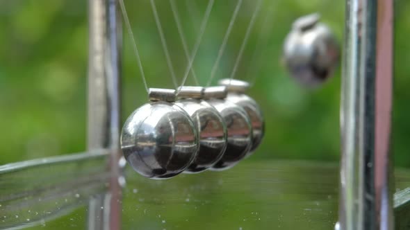 Newton's Cradle metal balls on green nature background, swinging metal balls, Macro shot. Close up. alt