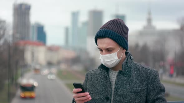 Man in Surgical Face Mask Uses Mobile App on Smartphone. Coronavirus Pandemic
