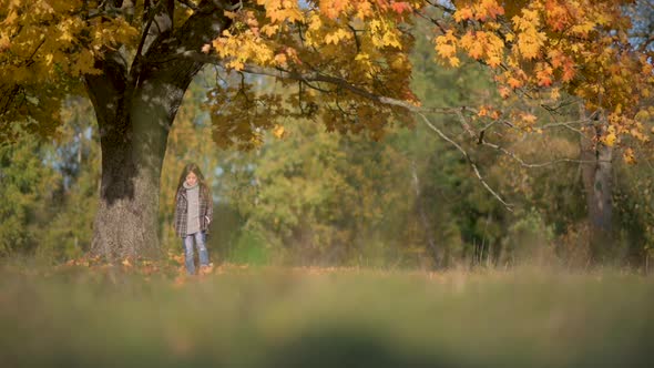 Happy Girl in Coat Walks in a Sunny Autumn Park.