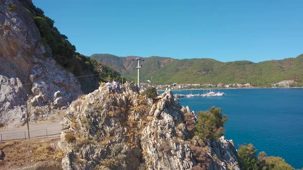 Young Couple Sits on a Rock on the Aegean Coast Against the Backdrop of Mountains and the Bay of alt