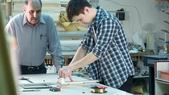 Young Trainee Trying To Cut a Glass for the Frame, Seniour Worker Watching alt