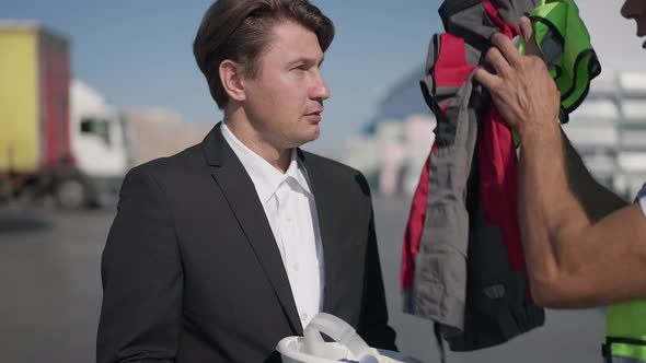 Portrait of Stressed Sad Caucasian Man in Suit Receiving Warehouse Uniform From Middle Eastern alt